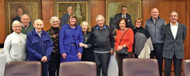 The Brandeis provost and a group of other people pose in front of portraits in the Brandeis trustees conference room